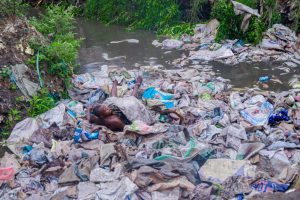 Un jeune homme complètement nu est plongé dans des déchets dans le caniveau qui conduit les eaux usées du dépotoir.